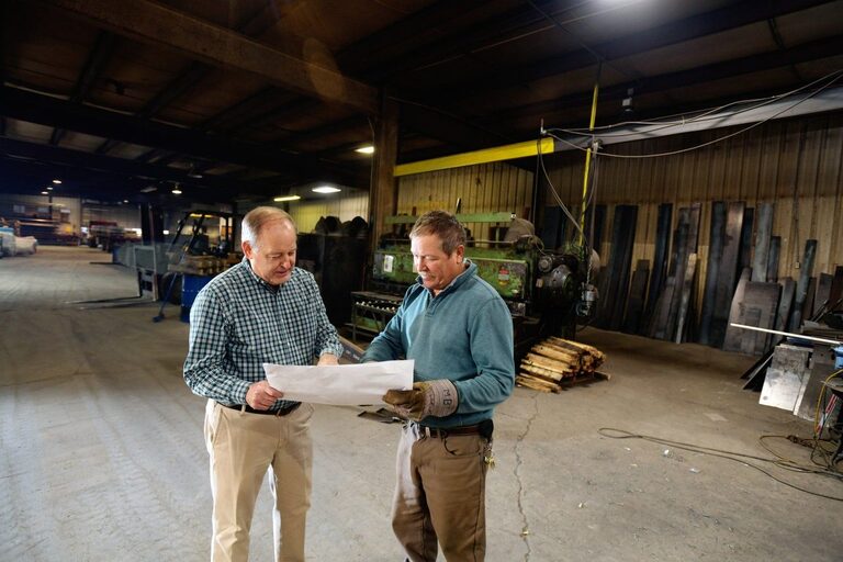Gex Williams reviewing plans with a man in a large workshop